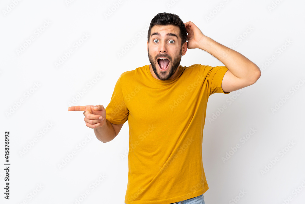 Young handsome man with beard isolated on white background surprised and pointing finger to the side