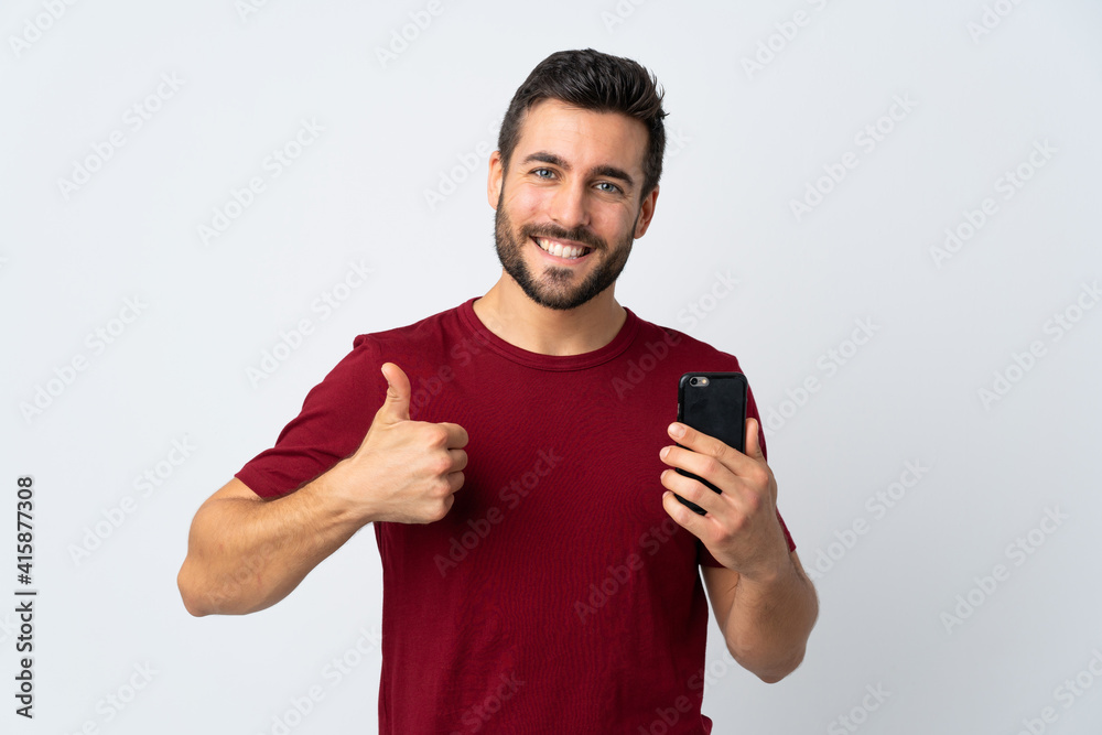 Young handsome man with beard using mobile phone isolated on white background with thumbs up because something good has happened Young handsome man with beard using mobile phone isolated on white background with thumbs up because something good has happened