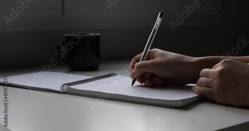 A right handed writing down a memo pad in front of a window in a tidy desk. 