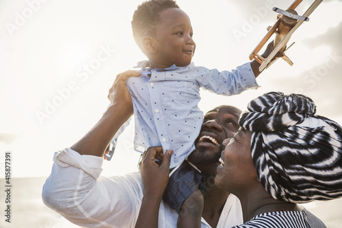 African parents and little son having fun with wood airplane on the beach - Family people and love concept - Focus on mother fave photo