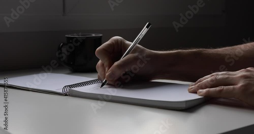 A right handed writing down a memo pad in front of a window in a tidy desk. 