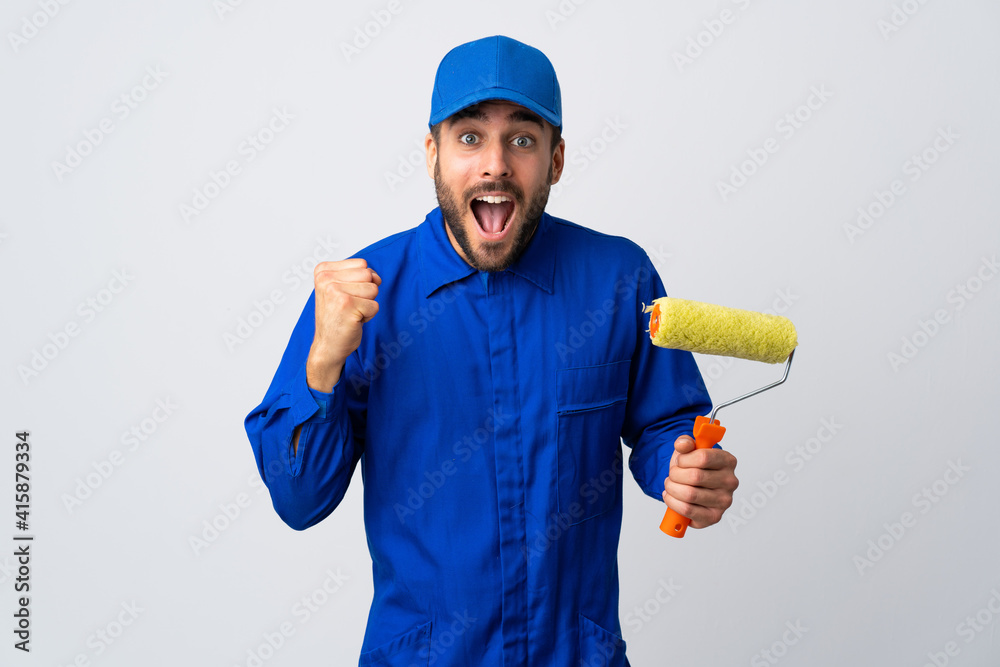 Painter man holding a paint roller isolated on white background celebrating a victory in winner position