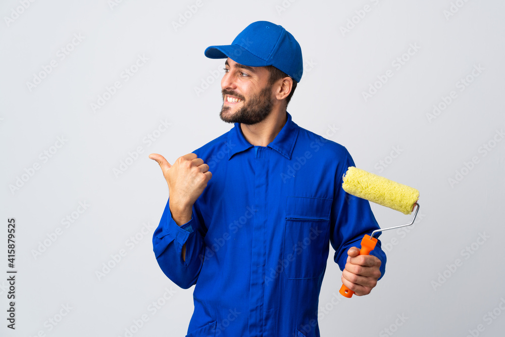 Painter man holding a paint roller isolated on white background pointing to the side to present a product