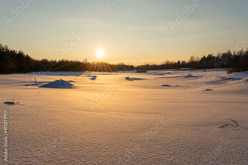 Snow dunes. The dark silhouette of the forest on the horizon. Winter evening landscape with sunset and orange multicolor sky.
