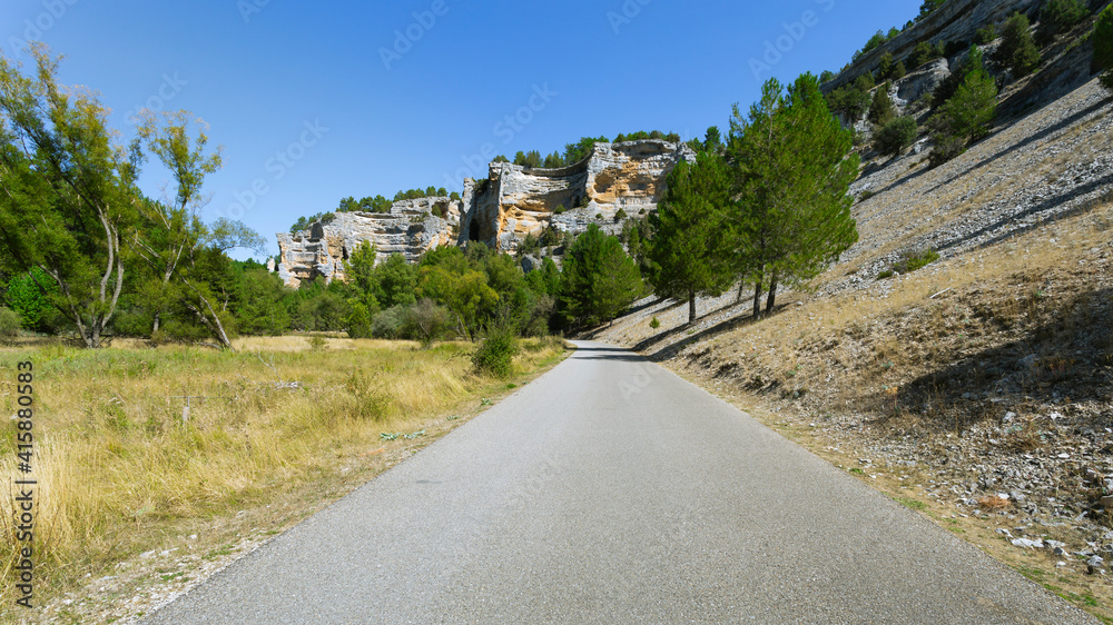 Road of the canyon of  Rio Lobos with green trees surrounding and walls of rocks in the background. Soria, Castilla y Leon, Spain