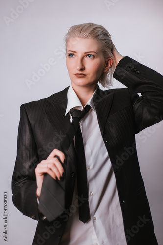 Fashionable portrait of a woman dressed in men's clothing. Girl in a white shirt, jacket and tie on a white background. The idea of a strong woman as a man.