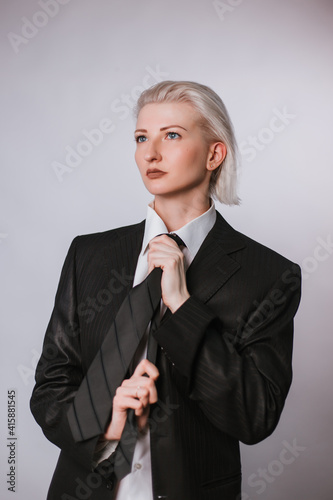 Fashionable portrait of a woman dressed in men's clothing. Girl in a white shirt, jacket and tie on a white background. The idea of a strong woman as a man.