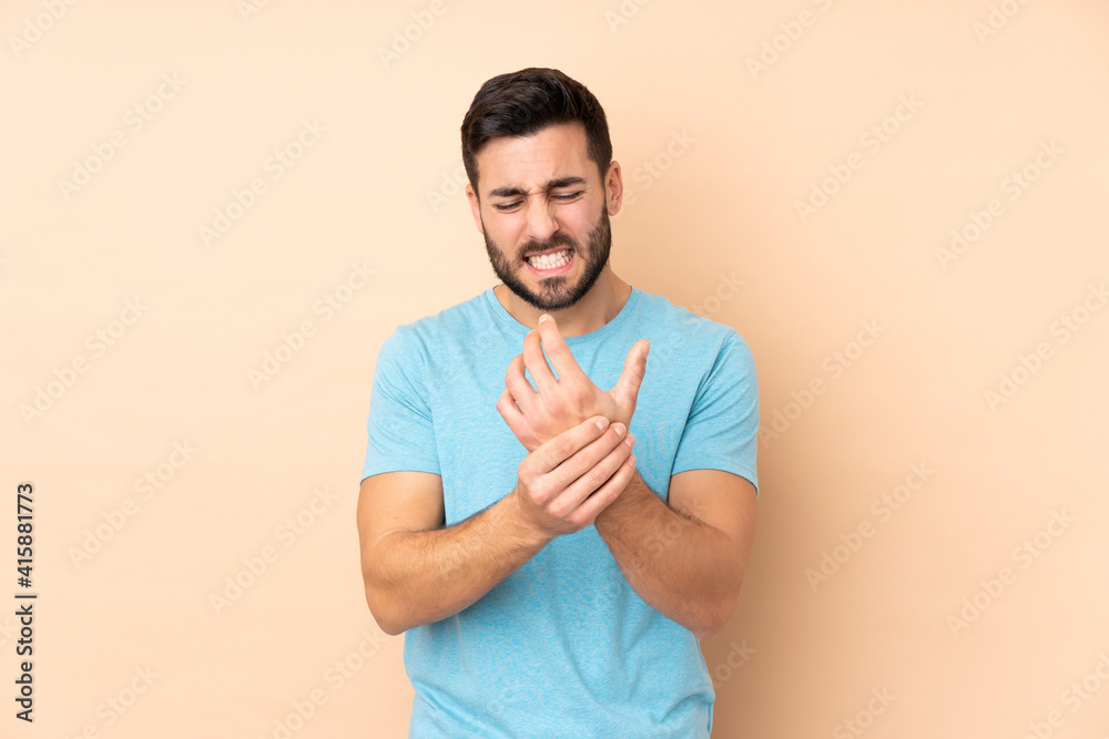 Caucasian handsome man isolated on beige background suffering from pain in hands Caucasian handsome man isolated on beige background suffering from pain in hands