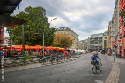 Canvas Print A woman rides a bicycles down a busy street past the Hackescher Markt square in