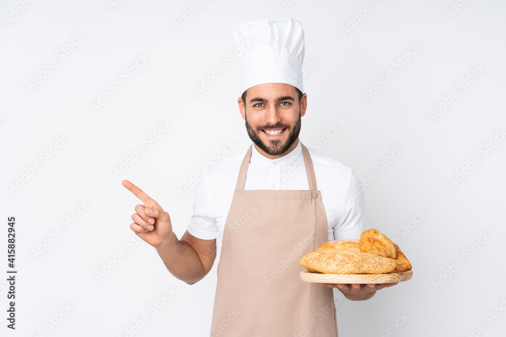 Male baker holding a table with several breads isolated on white background pointing finger to the side Male baker holding a table with several breads isolated on white background pointing finger to the side