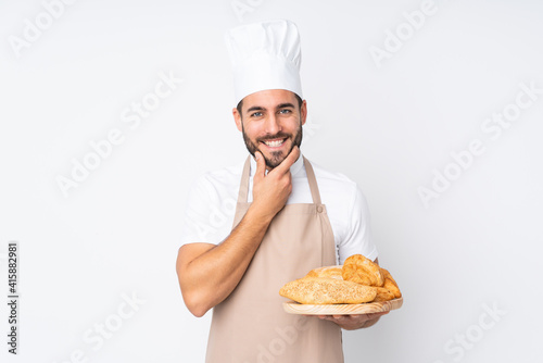 Male baker holding a table with several breads isolated on white background laughing