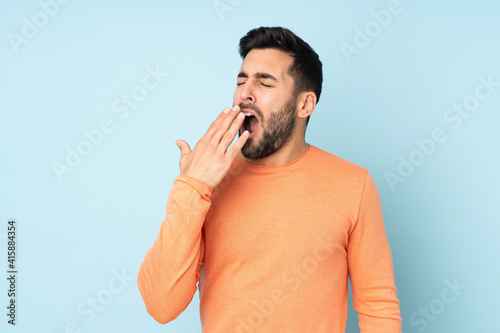 Caucasian handsome man yawning and covering wide open mouth with hand over isolated blue background photo