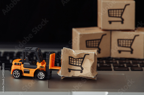 Orange forklift model and broken carton box on a keyboard close-up. Courier service and shipment accident concept.