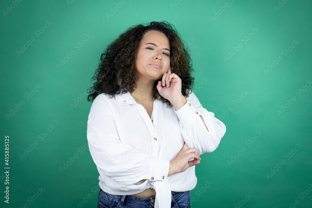 Young african american girl wearing white shirt over green background with hand on chin thinking about question, pensive expression. smiling and thoughtful face. doubt concept.