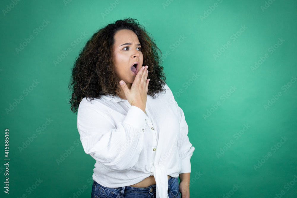 Young african american girl wearing white shirt over green background covering mouth with hand, shocked and afraid for mistake. surprised expression Young african american girl wearing white shirt over green background covering mouth with hand, shocked and afraid for mistake. surprised expression