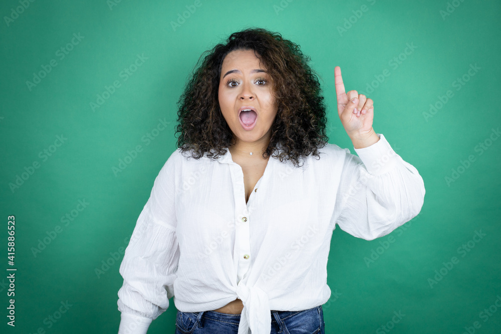 Young african american girl wearing white shirt over green background surprised and thinking with her finger on her head that she has an idea. Young african american girl wearing white shirt over green background surprised and thinking with her finger on her head that she has an idea.