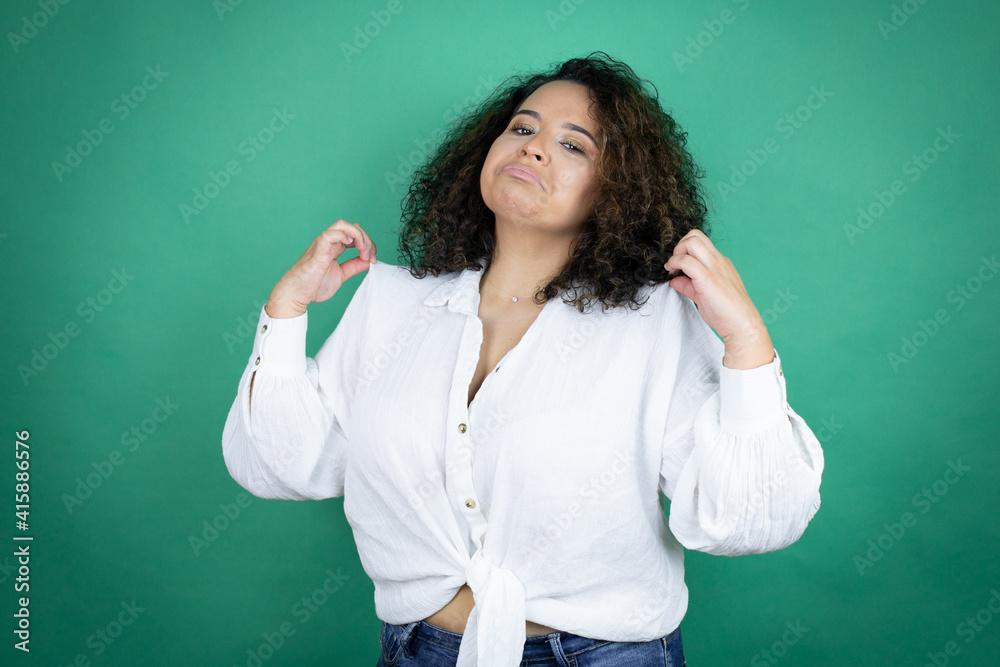 Young african american girl wearing white shirt over green background holding her t-shirt with a successful expression Young african american girl wearing white shirt over green background holding her t-shirt with a successful expression