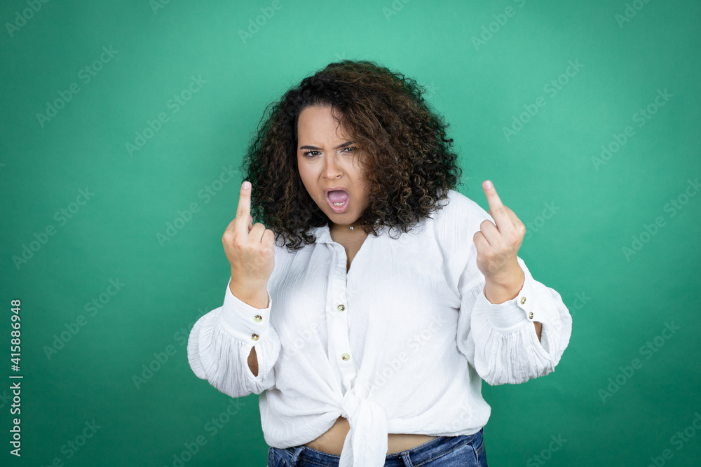 Young african american girl wearing white shirt over green background showing middle finger doing fuck you bad expression, provocation and rude attitude. screaming excited