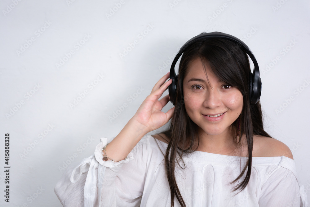beautiful smiling hispanic woman with long black hair wearing a black wireless headset with her hands gripping the headphones, isolated beautiful smiling hispanic woman with long black hair wearing a black wireless headset with her hands gripping the headphones, isolated