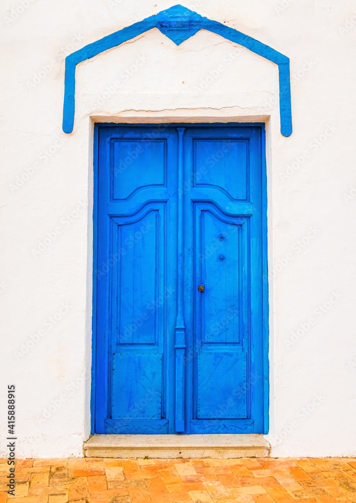 House with a beautiful blue wooden door, Mediterranean style, and an aged white facade.