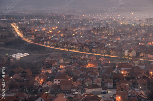 Night view of a cityscape with city and house lights  car light trails on a lighten road and misty  moody atmosphere