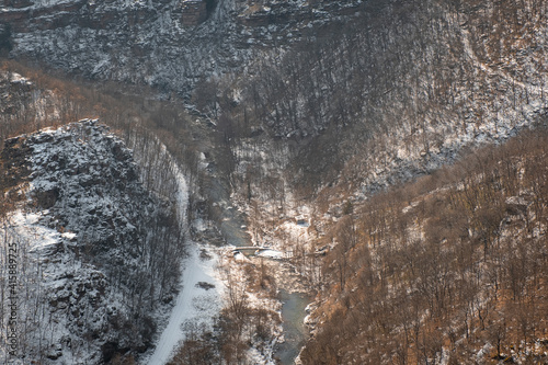 View from above of snow covered canyon and river surrounded by snow covered cliffs and orange trees photo