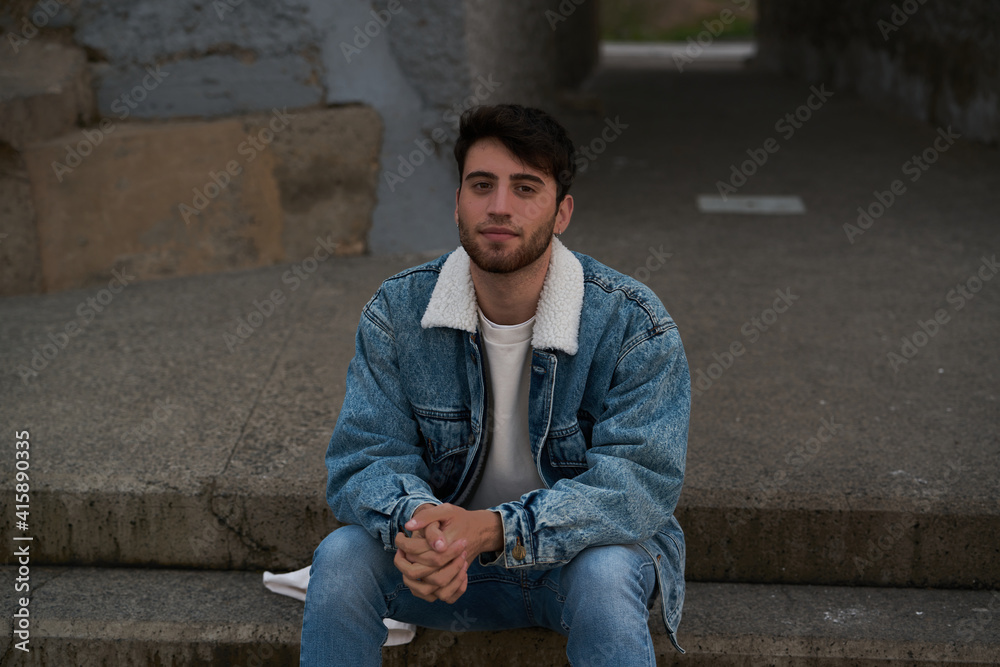 handsome student sitting in an urban setting on a beach in gran canaria late in the day at sunset