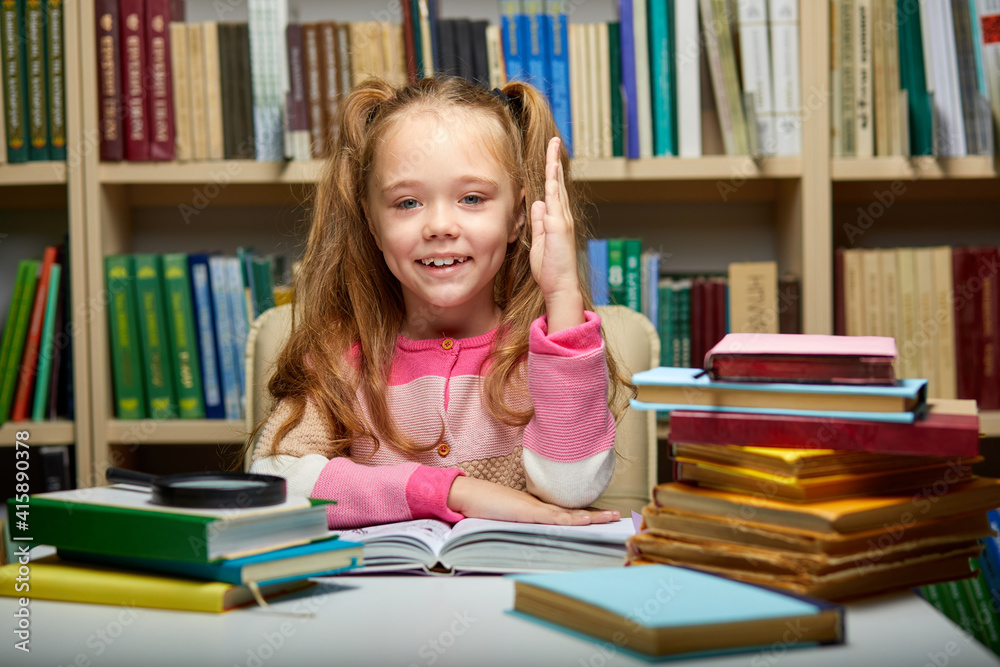 child girl raises her hand, knows the answers to all questions, erudite girl in library. education concept child girl raises her hand, knows the answers to all questions, erudite girl in library. education concept