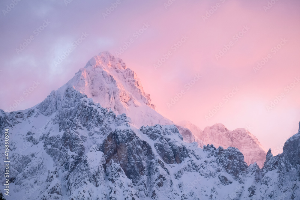 Beautiful close up shot of a pink glowing Mountain top in the Alps at sunset while wind is blowing snow off the Mountain. Power of natural elements in an alpine environment
