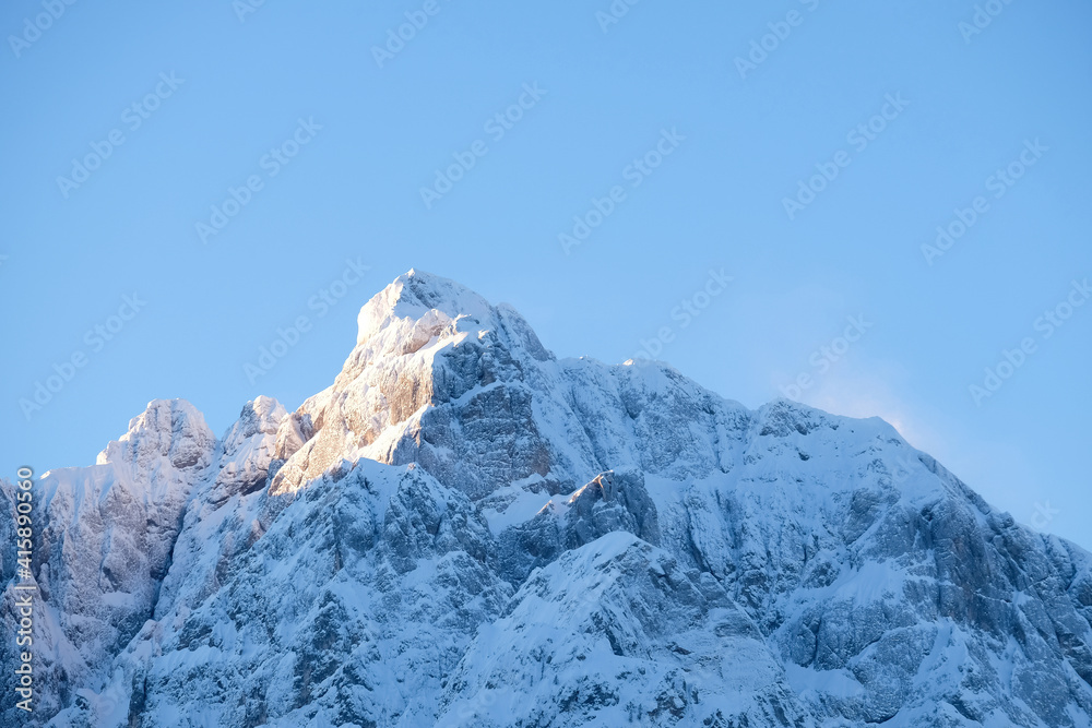 Beautiful close up shot of a pink glowing Mountain top in the Alps at sunset while wind is blowing snow off the Mountain. Power of natural elements in an alpine environment Beautiful close up shot of a pink glowing Mountain top in the Alps at sunset while wind is blowing snow off the Mountain. Power of natural elements in an alpine environment
