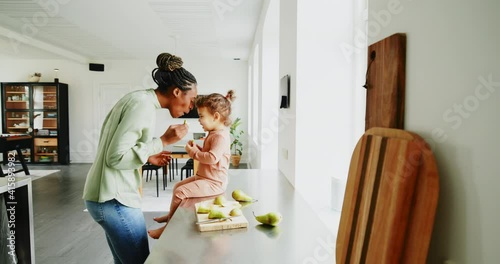 Loving young African mom and her adorable little daughter eating fruit together in their kitchen at home