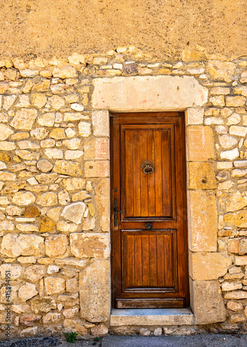 An old wooden door with a metal knocker and a stone frame and wall