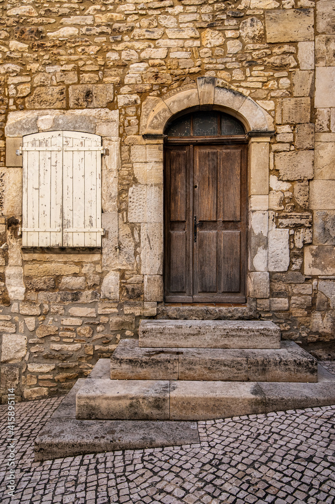 A very old vintage door with a stone wall and a white shuttered window