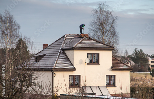 Billede på lærred A chimney sweep cleans the chimney on the roof of a detached house