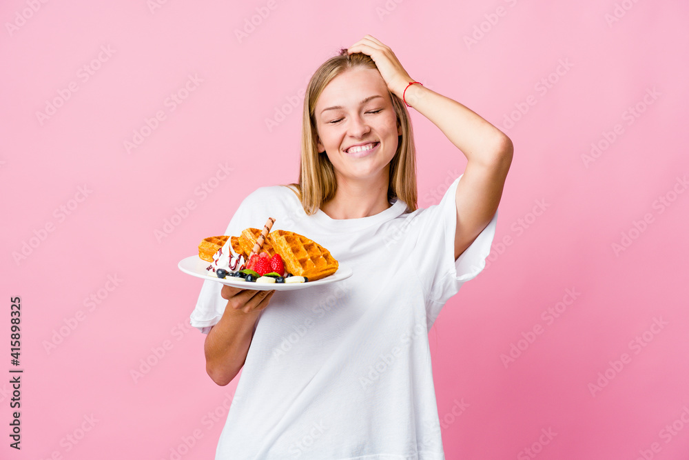Young russian woman eating a waffle isolated laughs joyfully keeping hands on head. Happiness concept. Young russian woman eating a waffle isolated laughs joyfully keeping hands on head. Happiness concept.