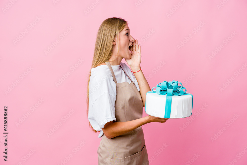 Young russian baker woman holding a delicious cake shouting and holding palm near opened mouth. Young russian baker woman holding a delicious cake shouting and holding palm near opened mouth.