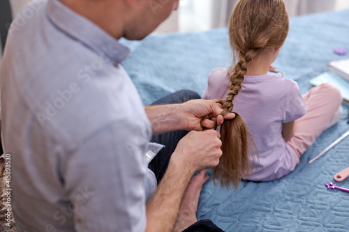 side profile photo father making braids to little girl in morning at home sitting on bed in domestic wear. family relationships, father day concept. close-up © alfa27