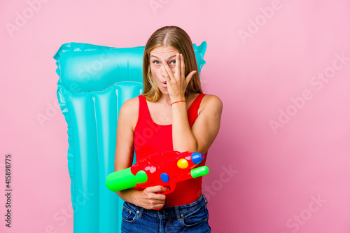 Young russian woman playing with a water gun with an air mattress blink through fingers frightened and nervous.
