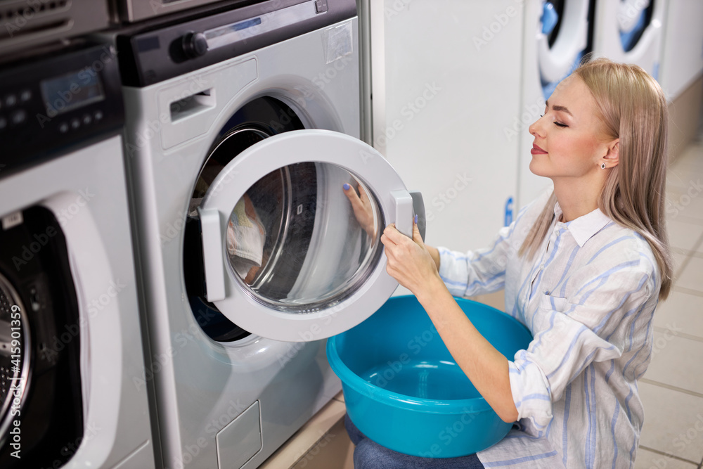 woman closes the washing machine, female is about to start washing after loading all things inside woman closes the washing machine, female is about to start washing after loading all things inside
