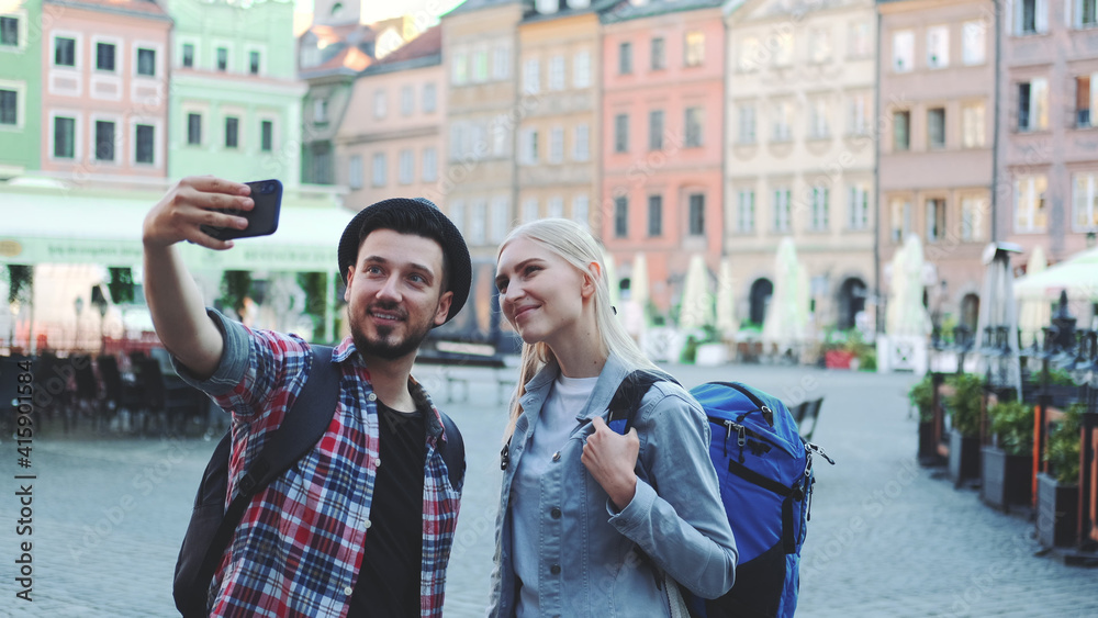 Happy young couple of tourists making selfie on smartphone in the city center. They have tourists bags.
