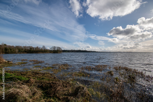 Lake view with low sky and swans swims in rough waters. Beautiful landscape with clouds over the lake.