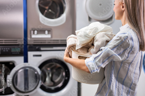 Foto woman doing laundry at laundry room with washing machine, holding basket with linen and towels in hands