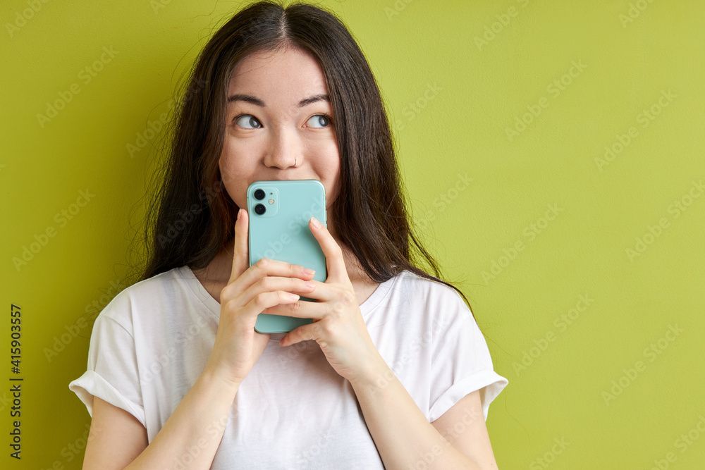 woman cheerfully reacting on message, holding smartphone in hands, hiding information in it, looking at side, isolated over green background woman cheerfully reacting on message, holding smartphone in hands, hiding information in it, looking at side, isolated over green background