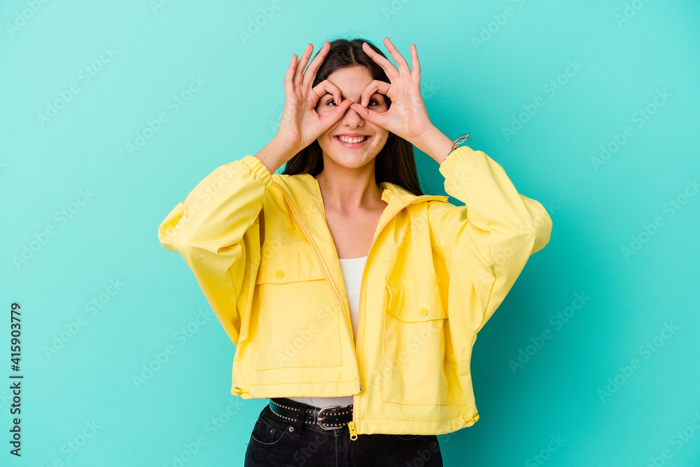 Young caucasian woman isolated on blue background showing okay sign over eyes Young caucasian woman isolated on blue background showing okay sign over eyes