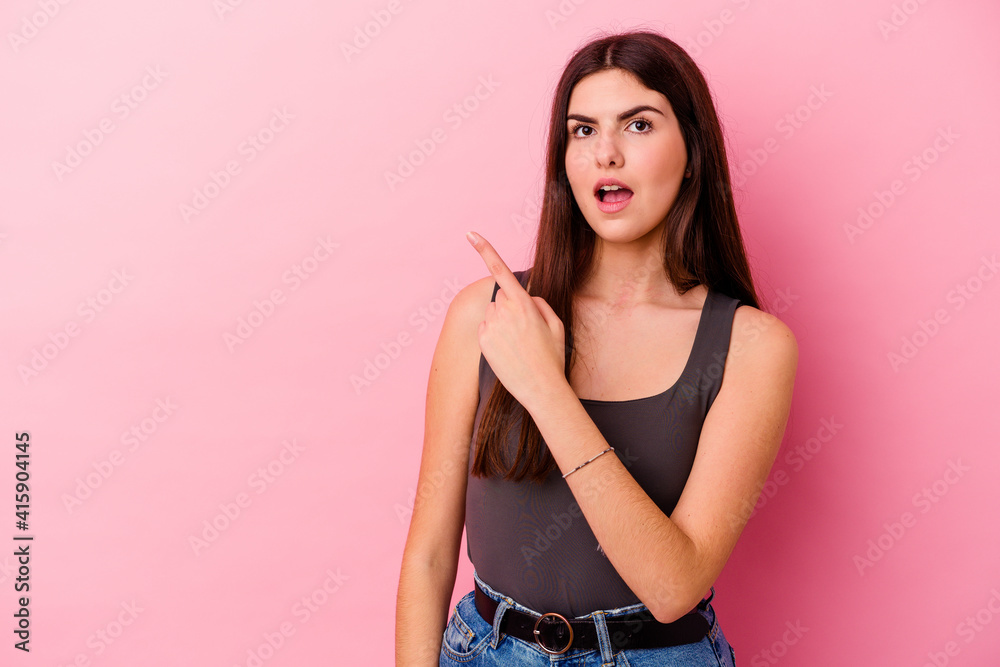 Young caucasian woman isolated on pink background pointing to the side
