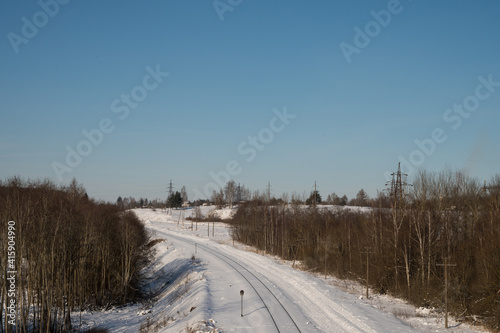 Snow-covered railway tracks between naked trees. Winter landscape. Sunny day. Blue sky.