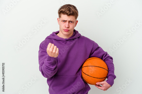 Young caucasian man playing basketball isolated background showing fist to camera, aggressive facial expression.