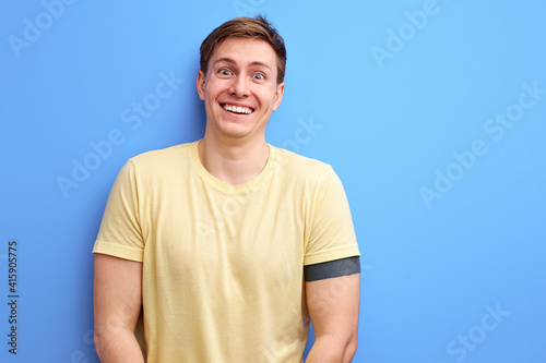positive male in casual t-shirt wear stands in contemplation, smiling. isolated over blue studio background. lifestyle, people, human emotions concept