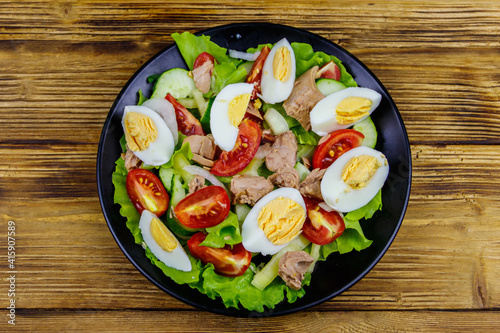 Tasty tuna salad with eggs, lettuce and fresh vegetables on wooden table. Top view