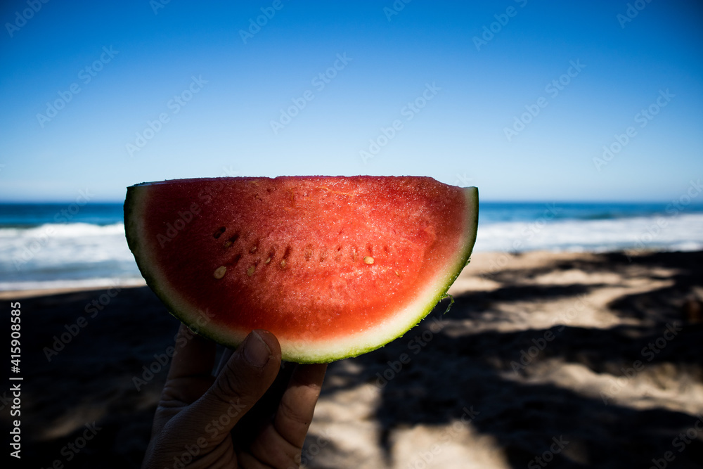 Hand holding a slice of watermelon to eat on the beach in Mexico Hand holding a slice of watermelon to eat on the beach in Mexico
